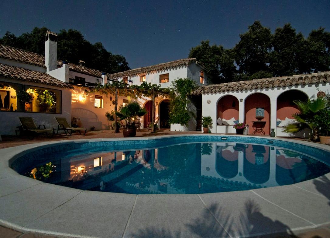 White Mediterranean villa with arched loggias around a lit swimming pool at night