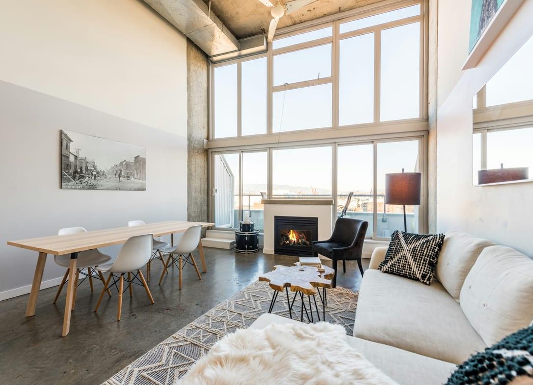 Double-height loft living room with tall windows, a fireplace, a long dining table and a white sofa