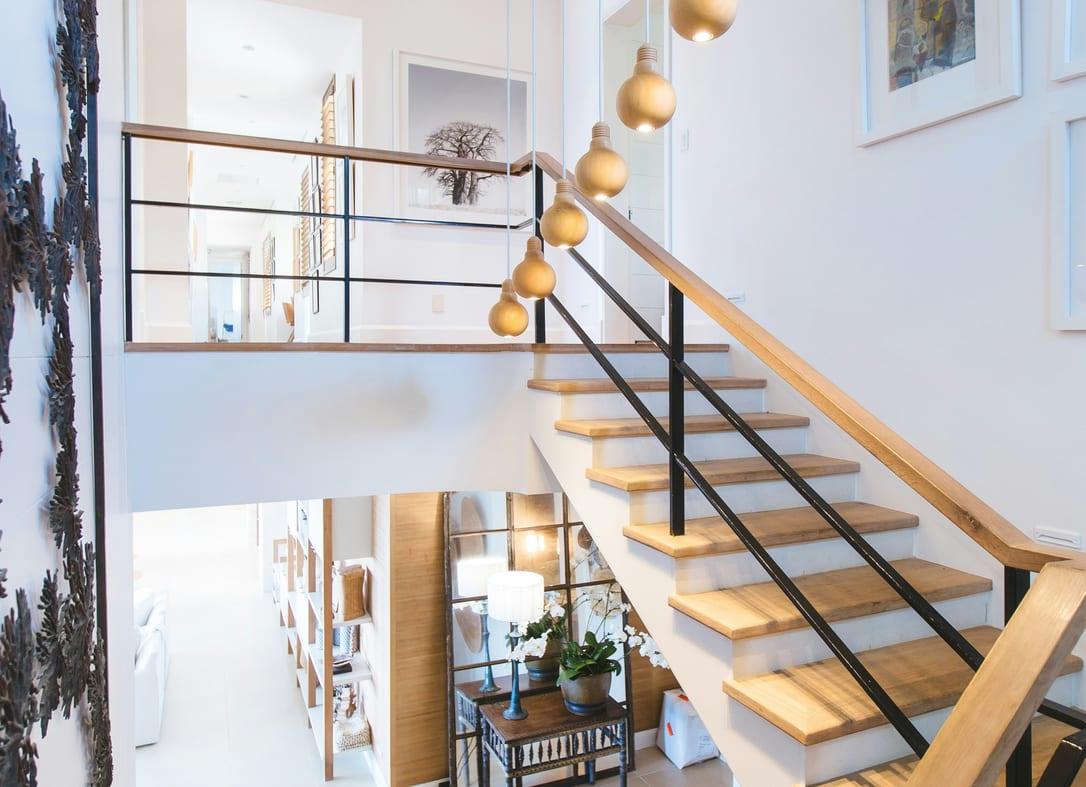 White stairwell with oak treads, black railings and brass pendant lights