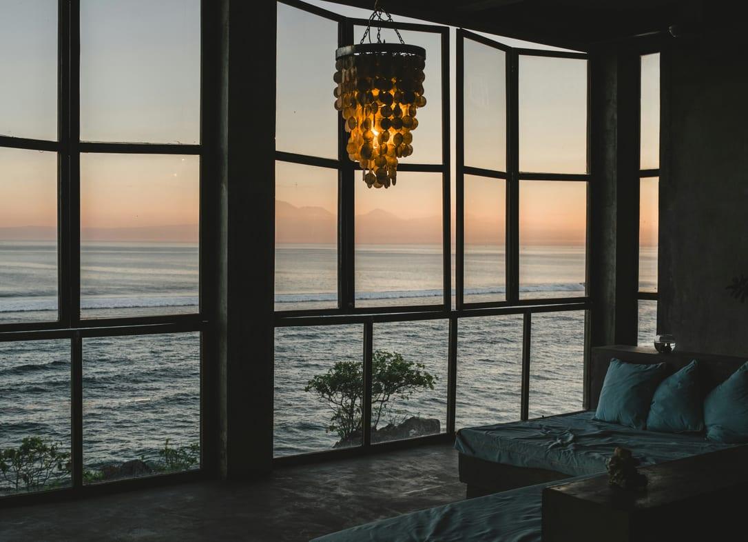 Dark penthouse living room at dusk with tall black-framed windows over the ocean and a hanging lamp