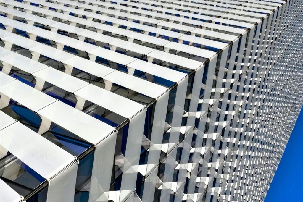 A white apartment tower with a grid of deep balconies against a blue sky