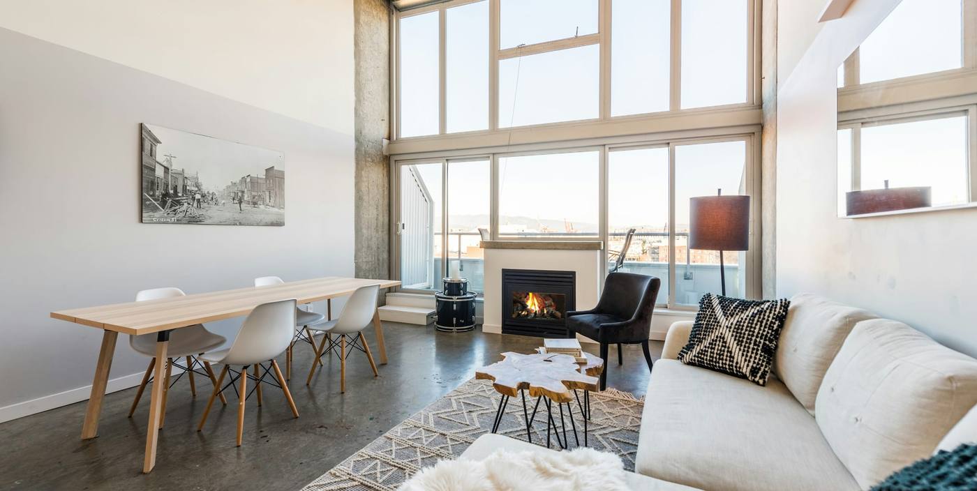 Double-height loft living room with tall windows, a fireplace, a long dining table and a white sofa