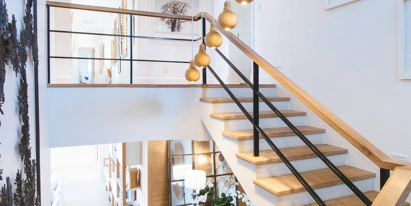 White stairwell with oak treads, black railings and brass pendant lights