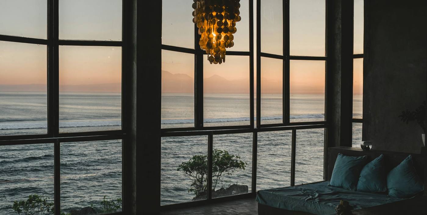 Dark penthouse living room at dusk with tall black-framed windows over the ocean and a hanging lamp