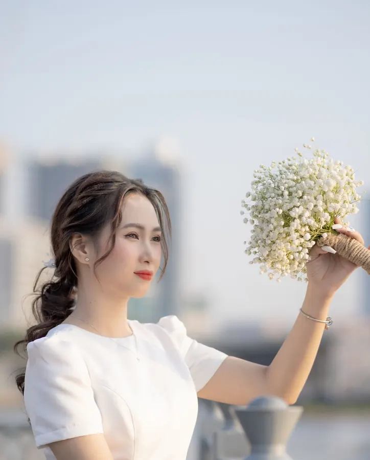 Mai raising her bouquet of baby&rsquo;s breath by the river