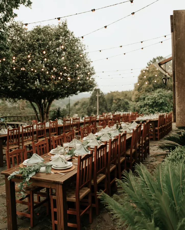 Long wooden tables set for dinner in a garden, strings of lights overhead