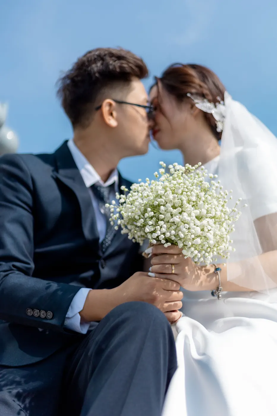 The couple kissing on the steps of the bridge, her bouquet of baby’s breath between them