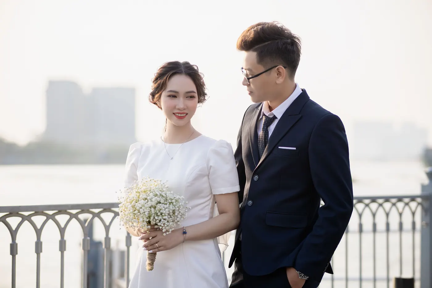Mai with her bouquet and Khoa in his navy suit, looking at each other by the river