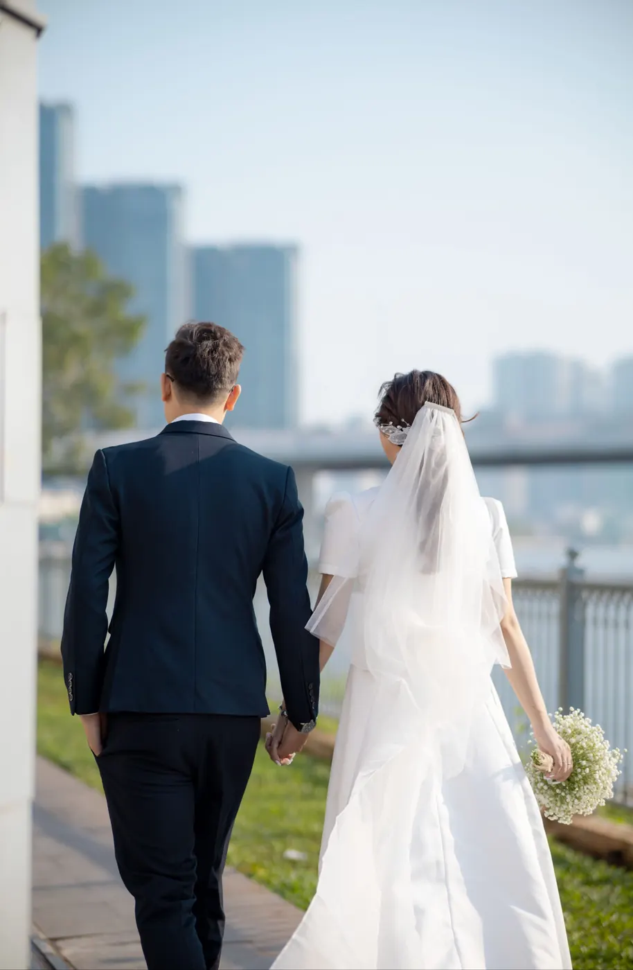 The couple walking away from the camera along the bridge, her veil trailing