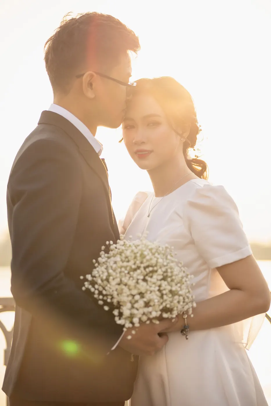 Mai and Khoa kissing against the low evening sun by the river
