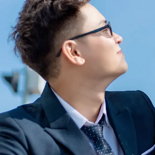 Khoa in glasses and a navy suit, looking up and smiling