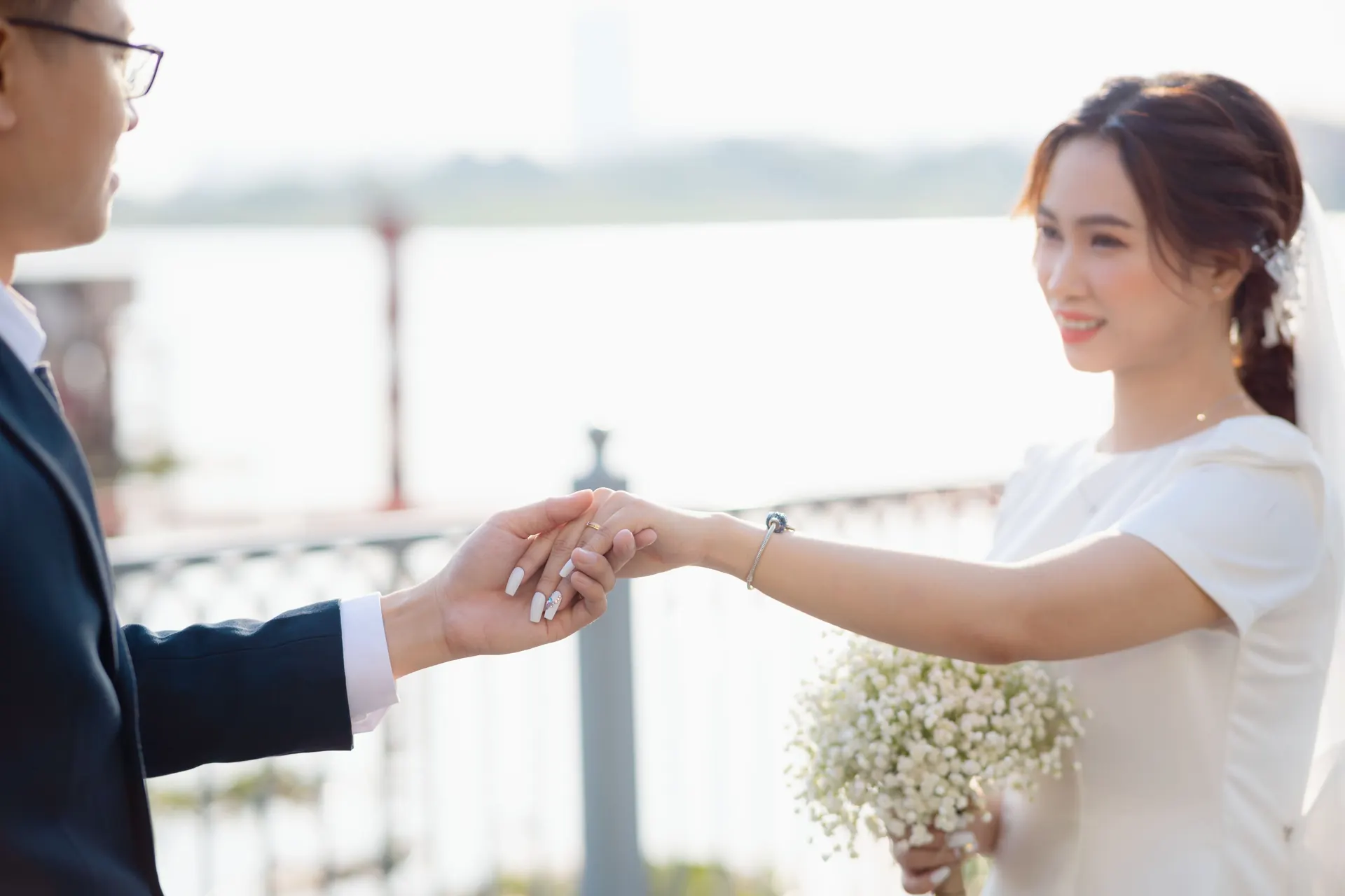 Khoa holding out his hand to Mai by the river; she smiles, a bouquet of baby&rsquo;s breath in her other hand