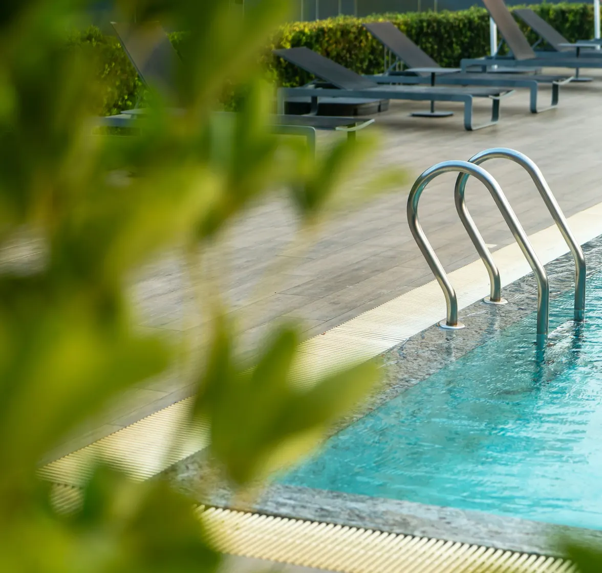 Steps into the clear blue water of a hotel pool, loungers beyond and leaves in the foreground