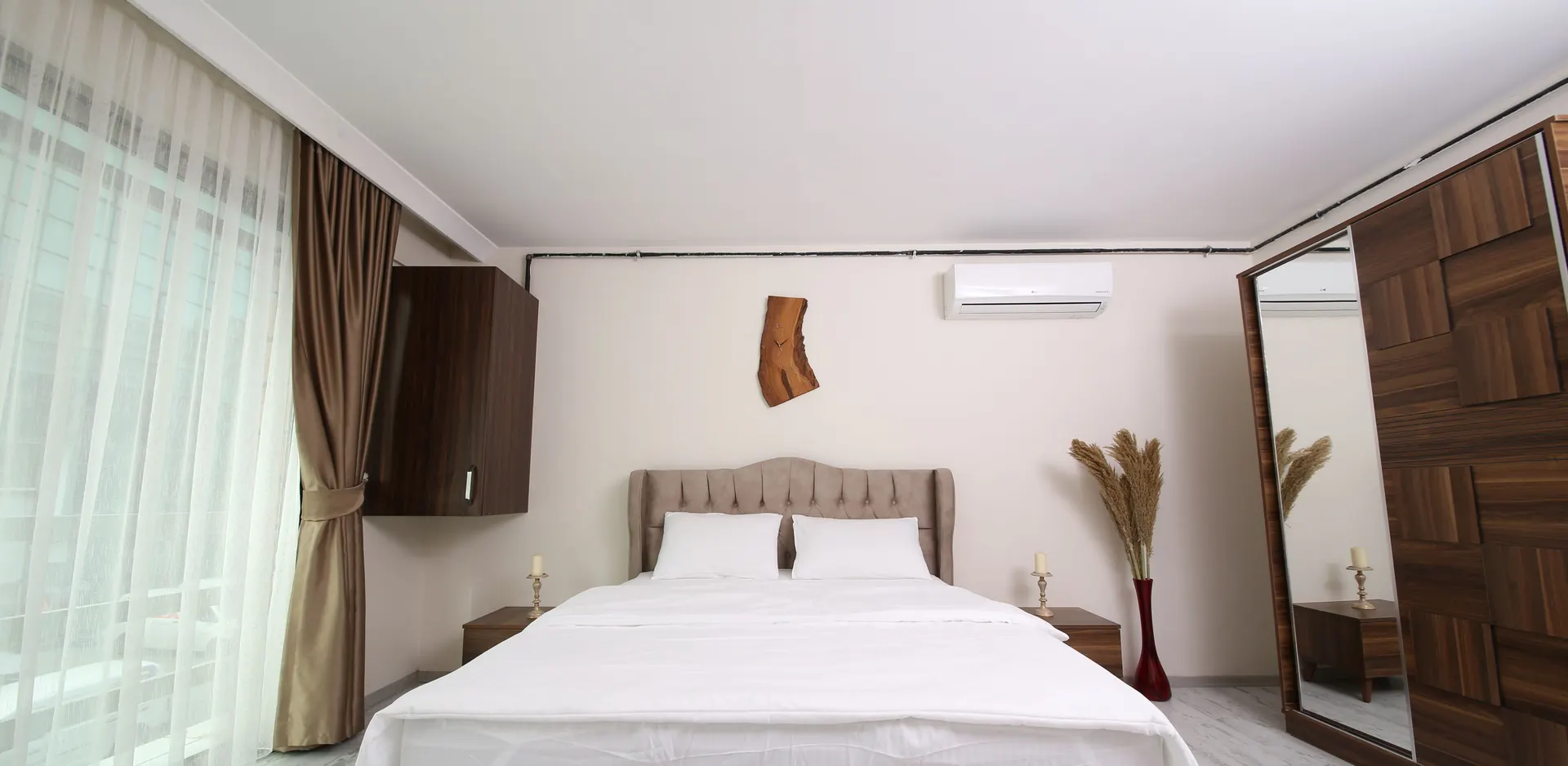 A bright hotel room with a double bed made up in white, long curtains at the window