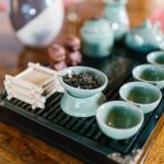 A pale green tea set on a wooden tray: a small pot, cups on a slatted board, loose tea in a dish