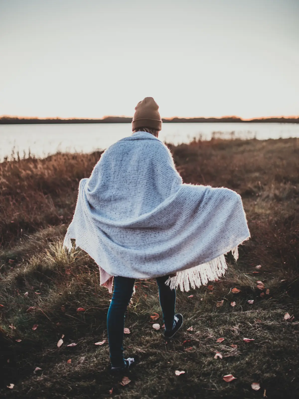 A woman walking through a field wrapped in a pale blue blanket scarf