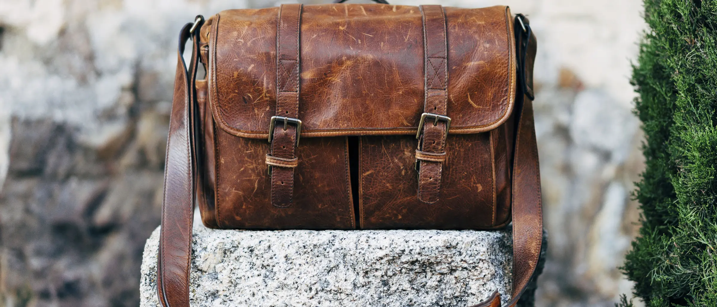 A brown leather messenger bag resting on a stone wall