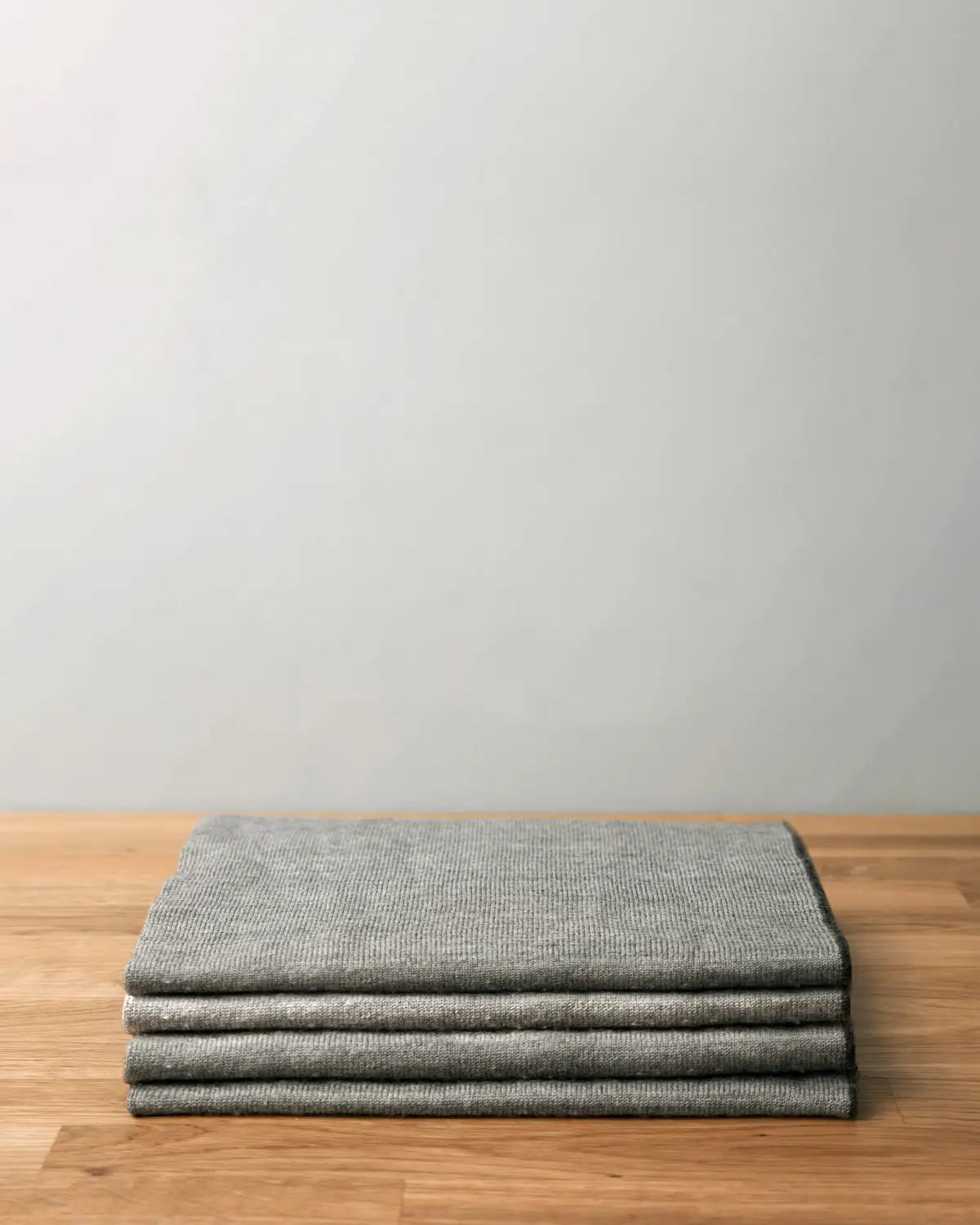 Folded grey knitwear stacked on an oak table