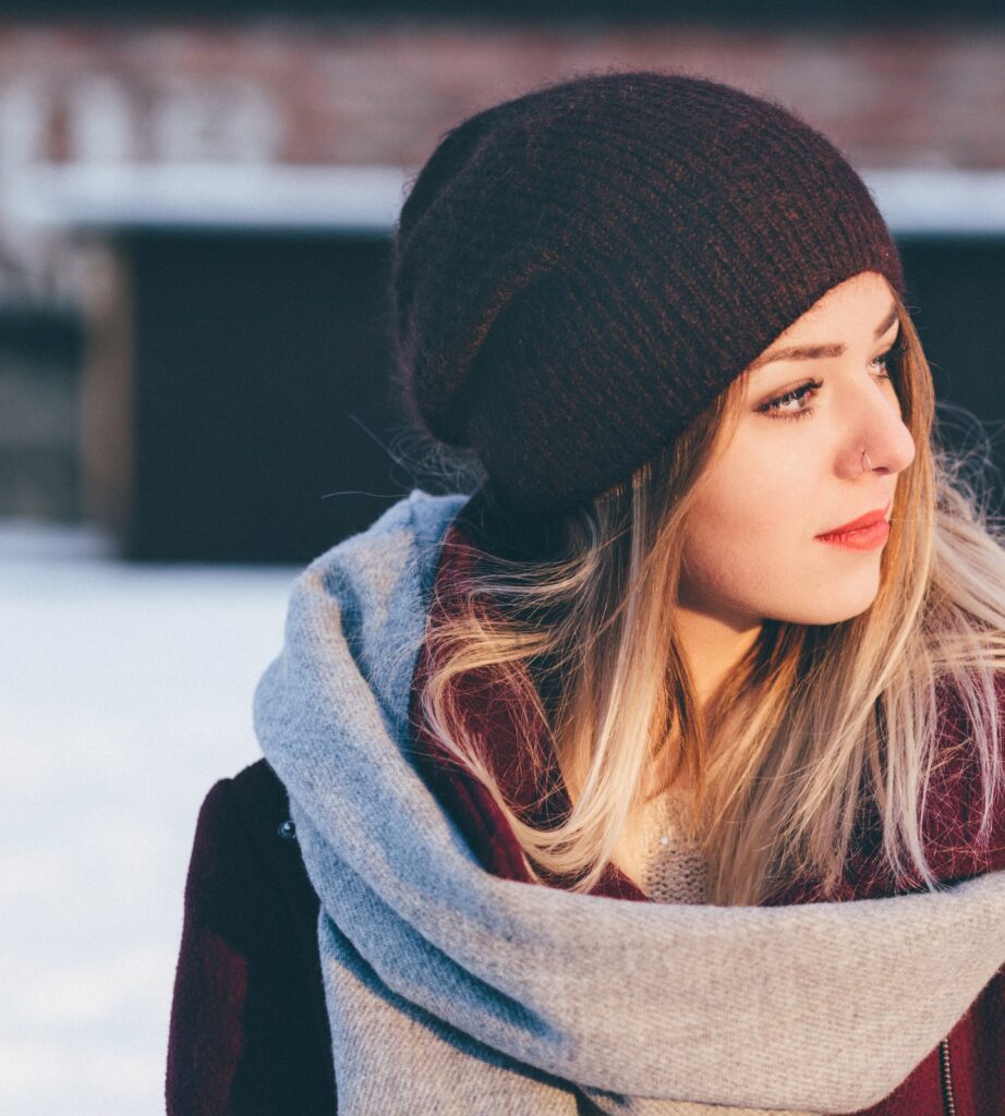 A woman in a burgundy wool coat, grey scarf and knitted beanie in the snow