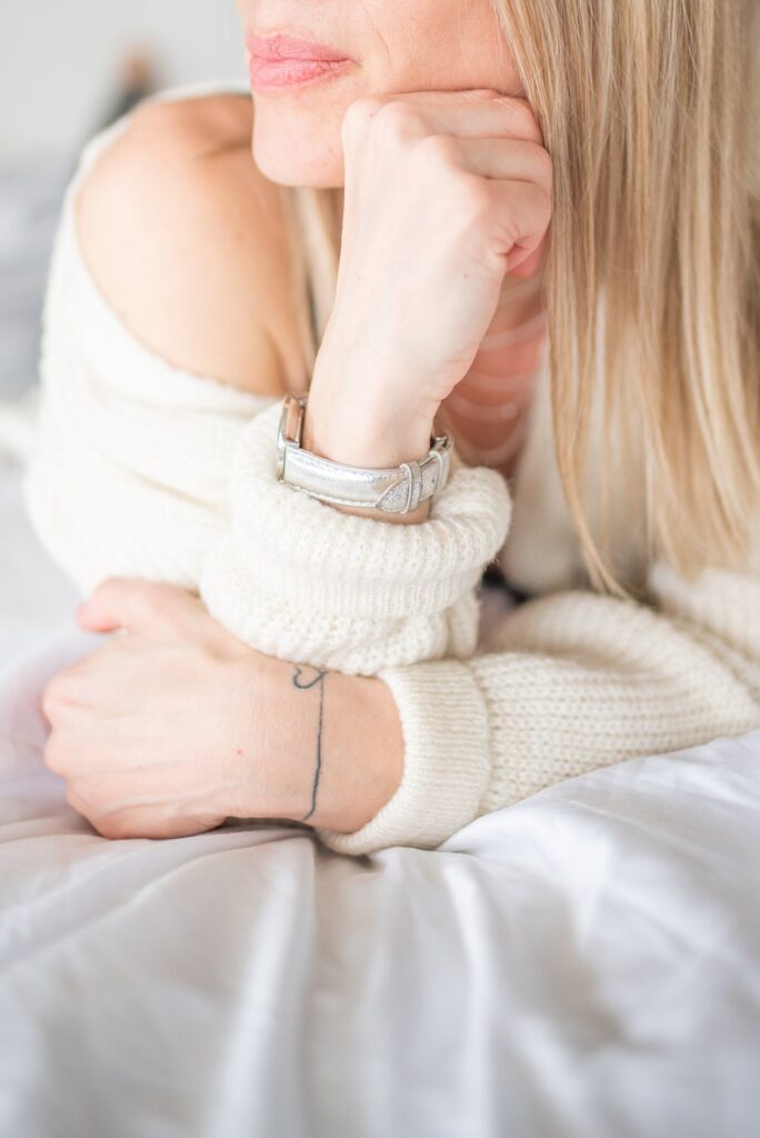 A woman in a cream chunky knit jumper resting on white linen
