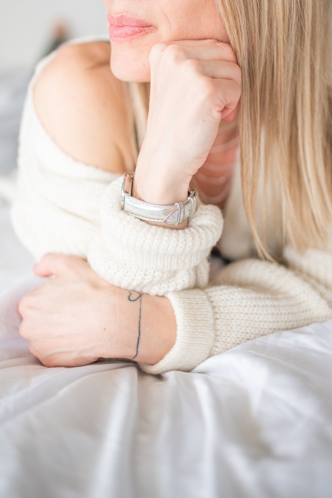 A woman in a cream chunky knit jumper resting on white linen