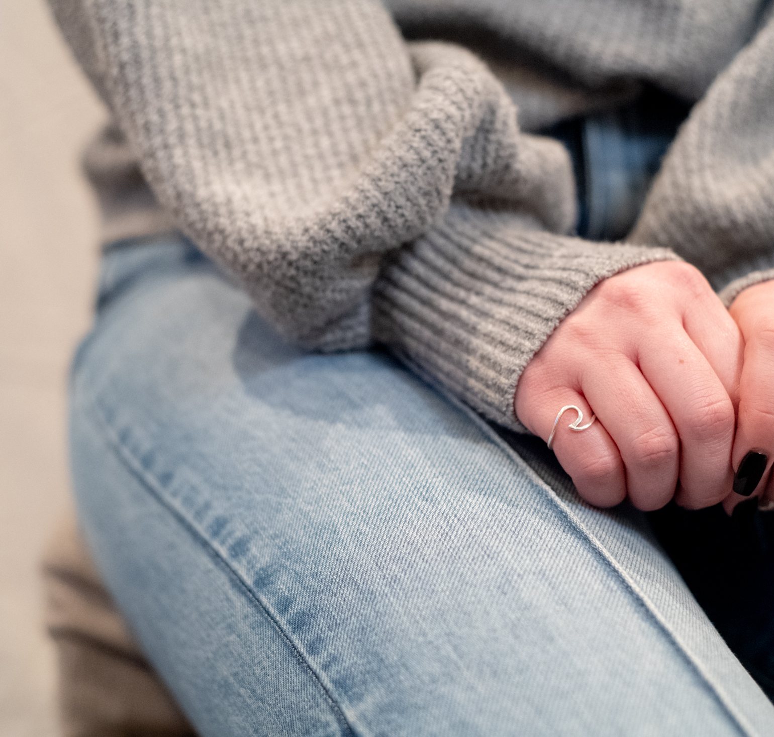 Hands resting on jeans in a grey knit sweater