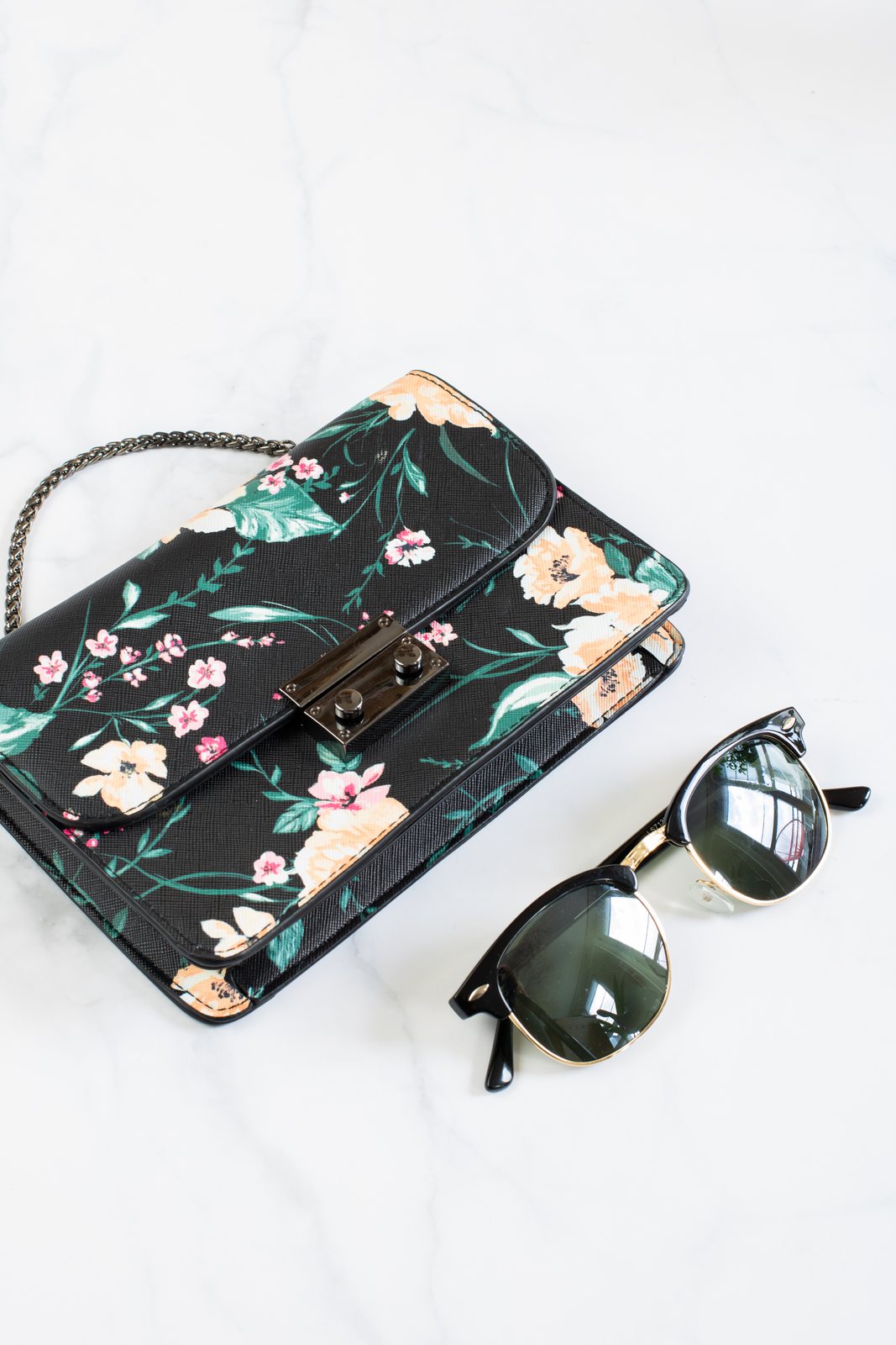 A black floral bag with a gold chain strap beside sunglasses