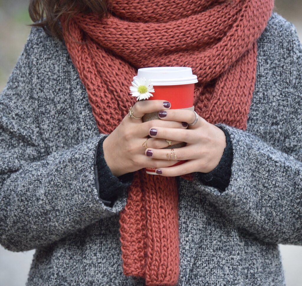 Hands holding a coffee cup against a grey wool coat and rust scarf