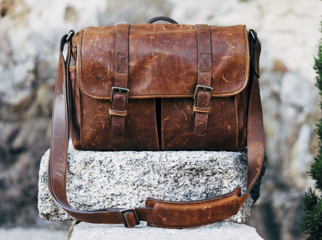A brown leather messenger bag resting on a stone wall