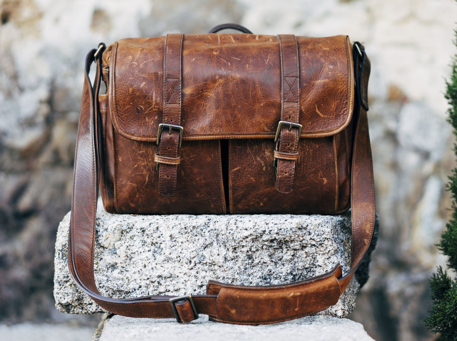 A brown leather messenger bag resting on a stone wall
