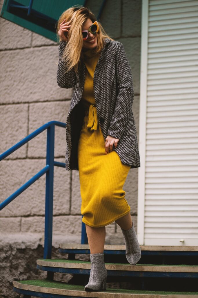A woman in a mustard knit dress and tweed coat on a stairway