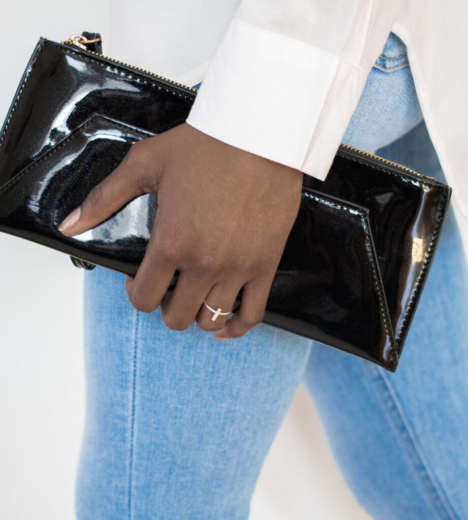 A black patent clutch held against blue jeans