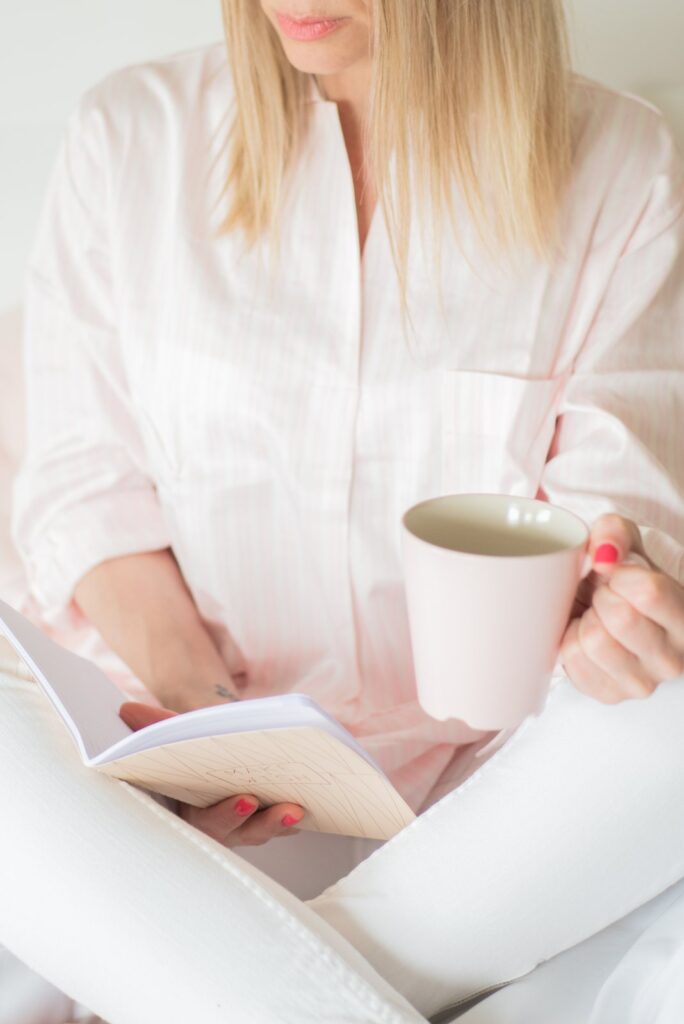 A woman in a pale pink blouse reading with a mug of tea