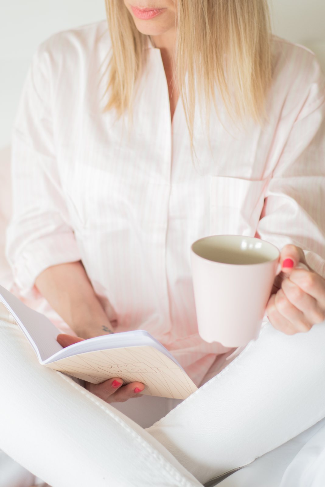 A woman in a pale pink blouse reading with a mug of tea