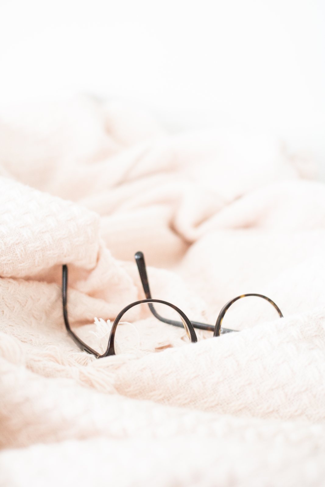 Round wire-frame glasses resting on a soft blush blanket