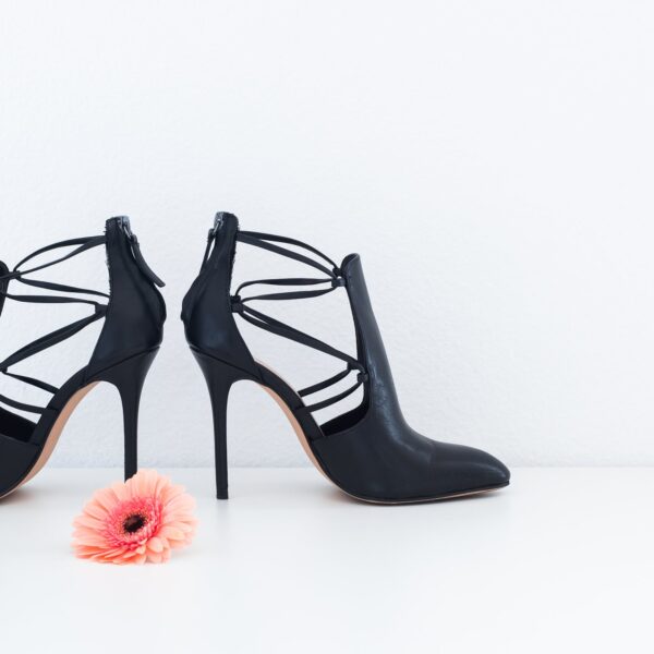 Black strappy heeled ankle boots on a white floor