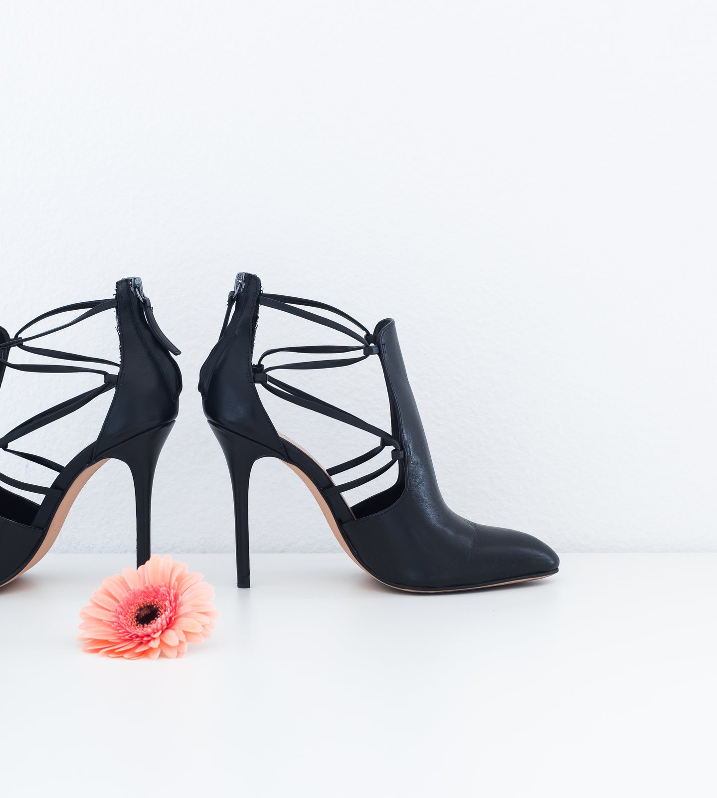 Black strappy heeled ankle boots on a white floor