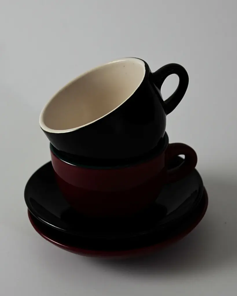 Two stacked cups and saucers in black and deep red