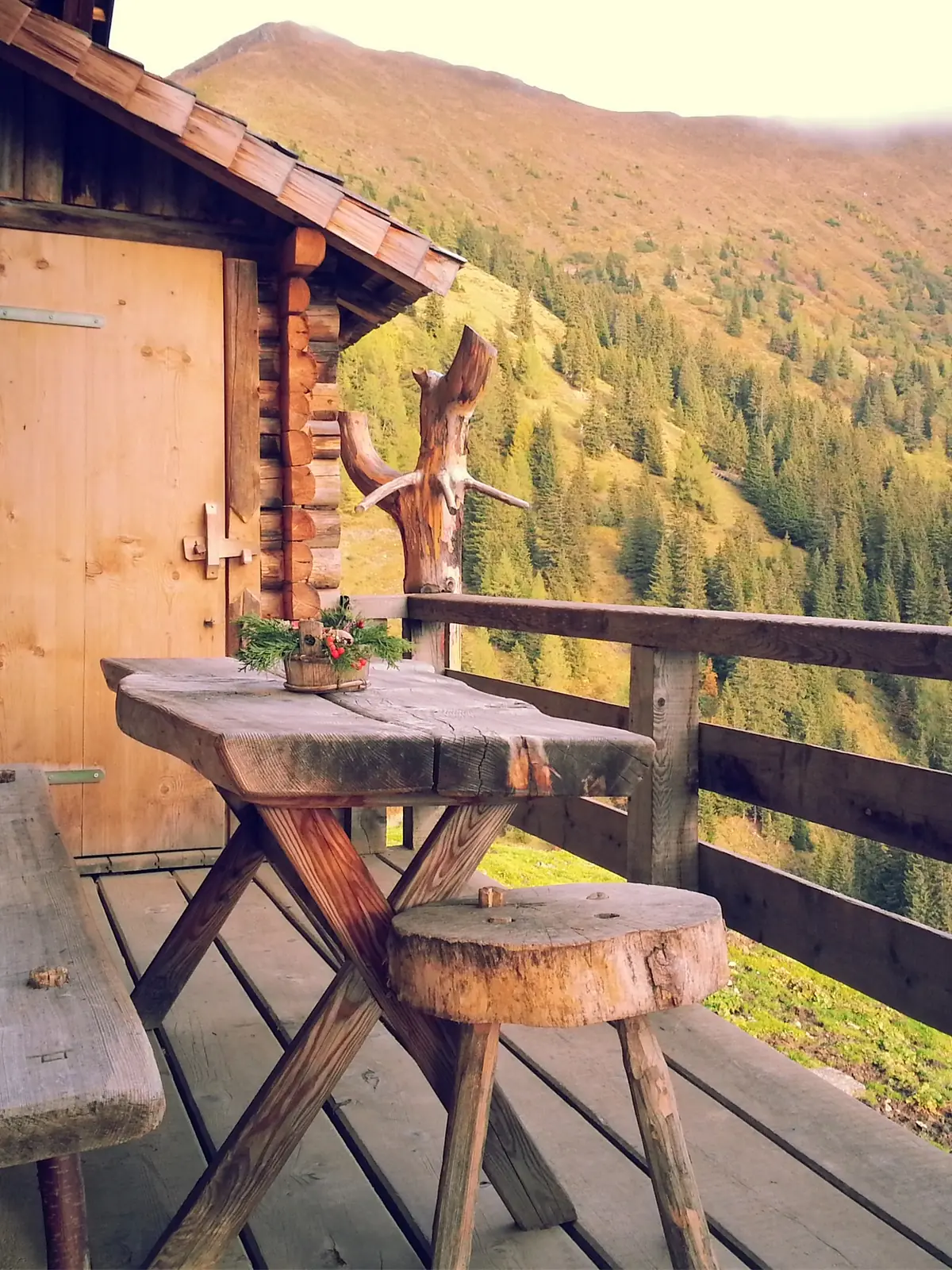 A rustic timber table and stools on a balcony above a wooded valley