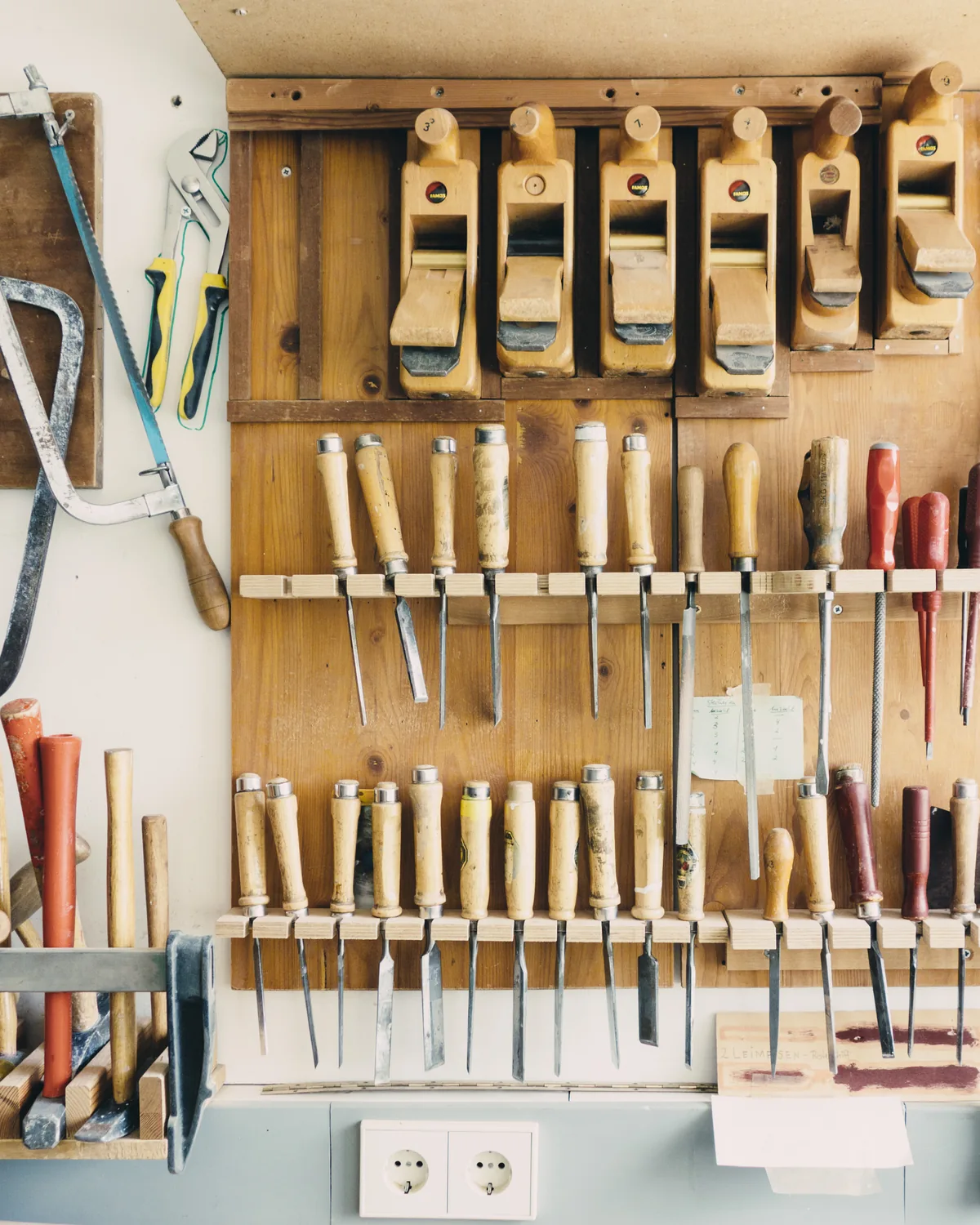 A workshop pegboard hung with chisels, clamps and saws