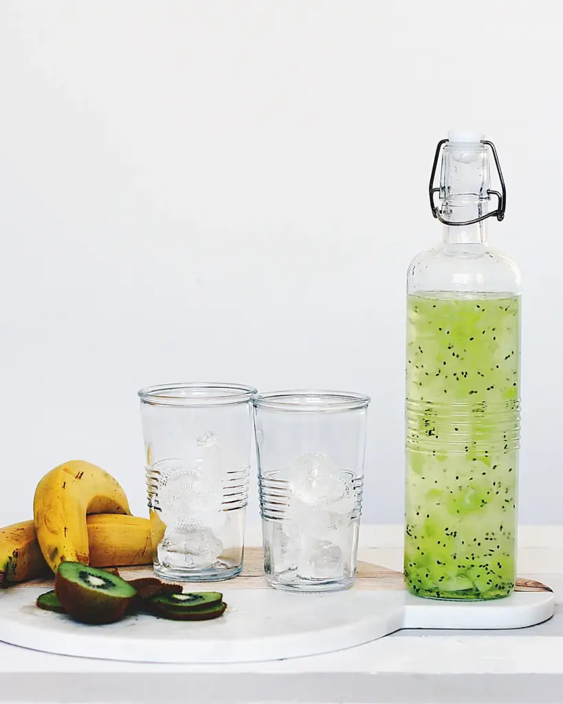 A bottle of green juice with glasses and citrus