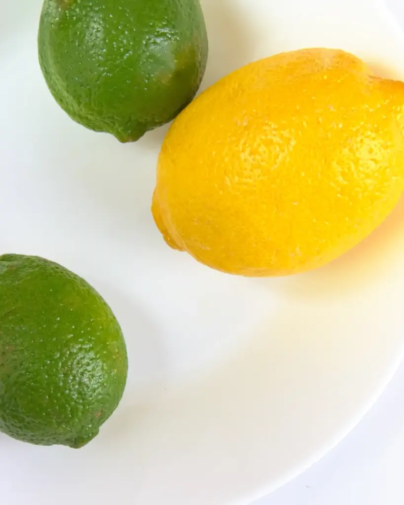 Lemons and limes, halved and whole, on a white plate
