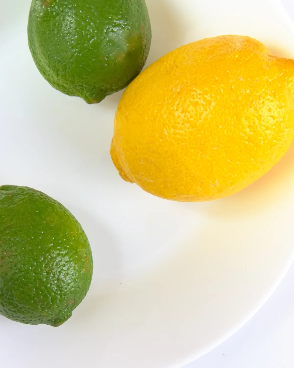 Lemons and limes, halved and whole, on a white plate