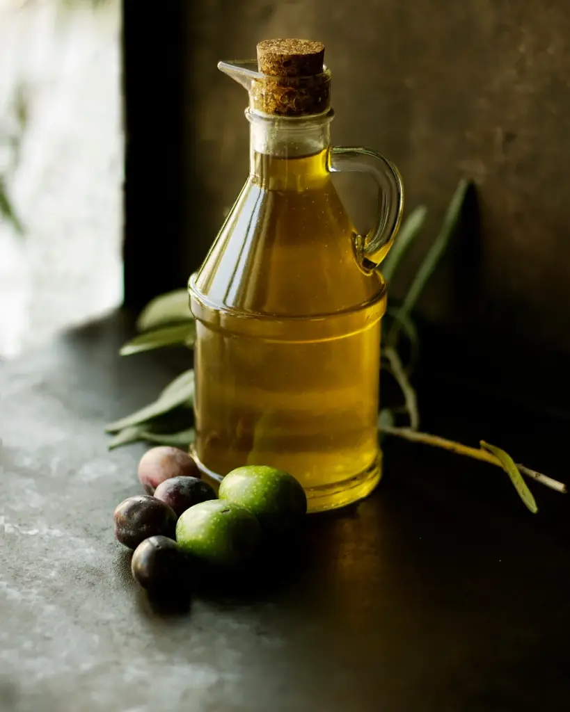 A bottle of olive oil with olives and herbs