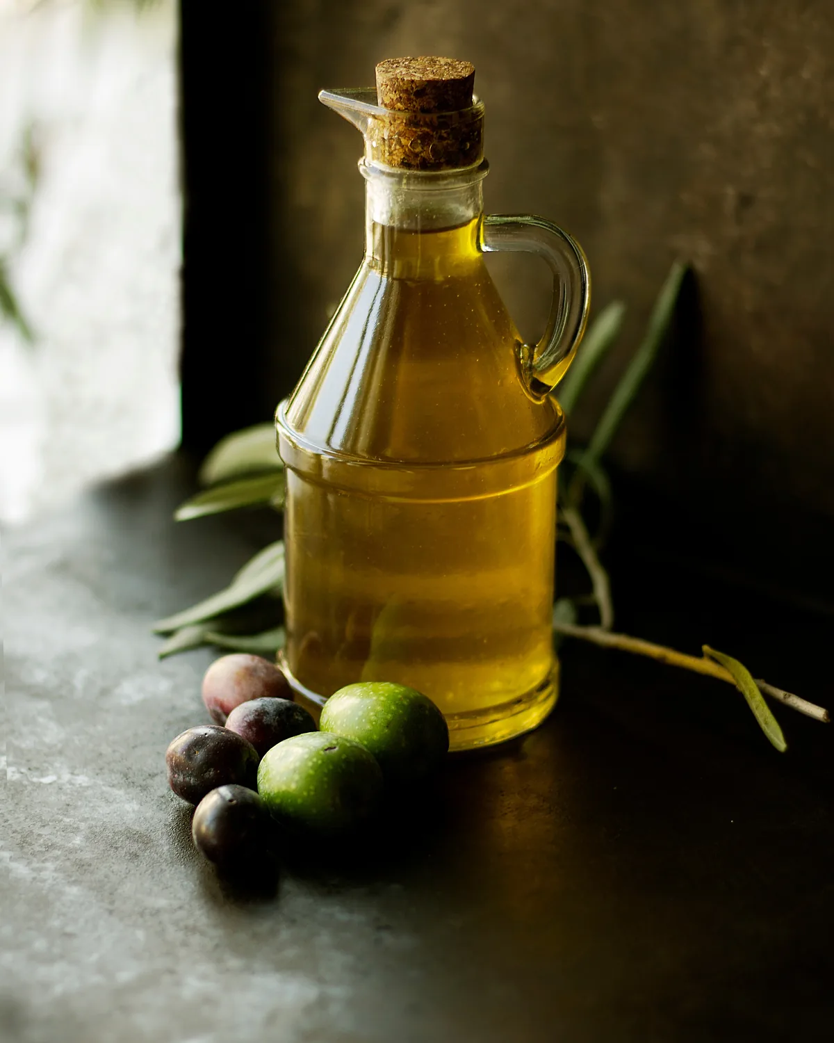 A bottle of olive oil with olives and herbs