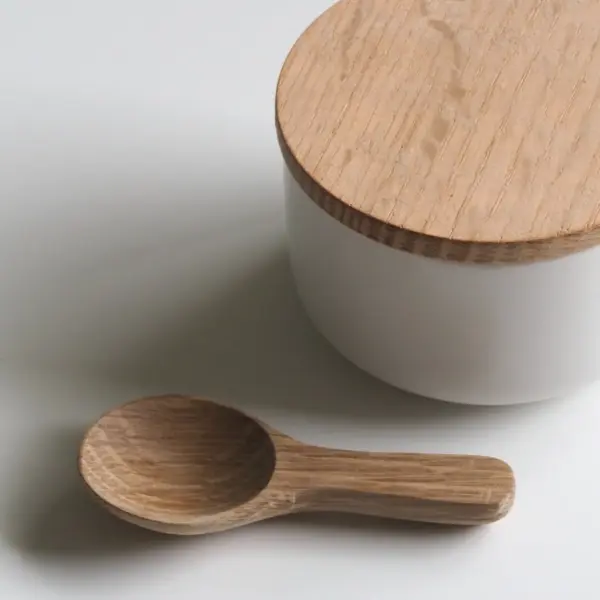 A plain white ceramic canister with a pale wooden lid