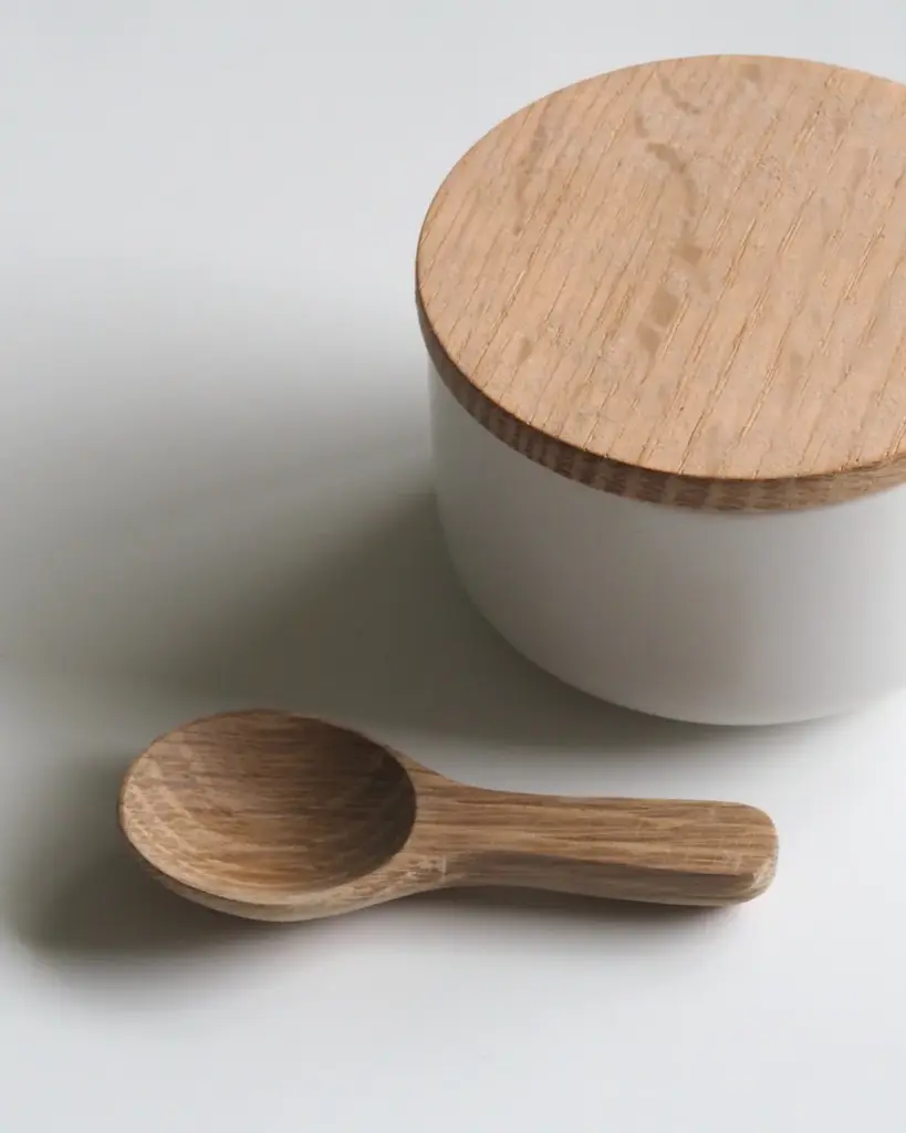 A plain white ceramic canister with a pale wooden lid
