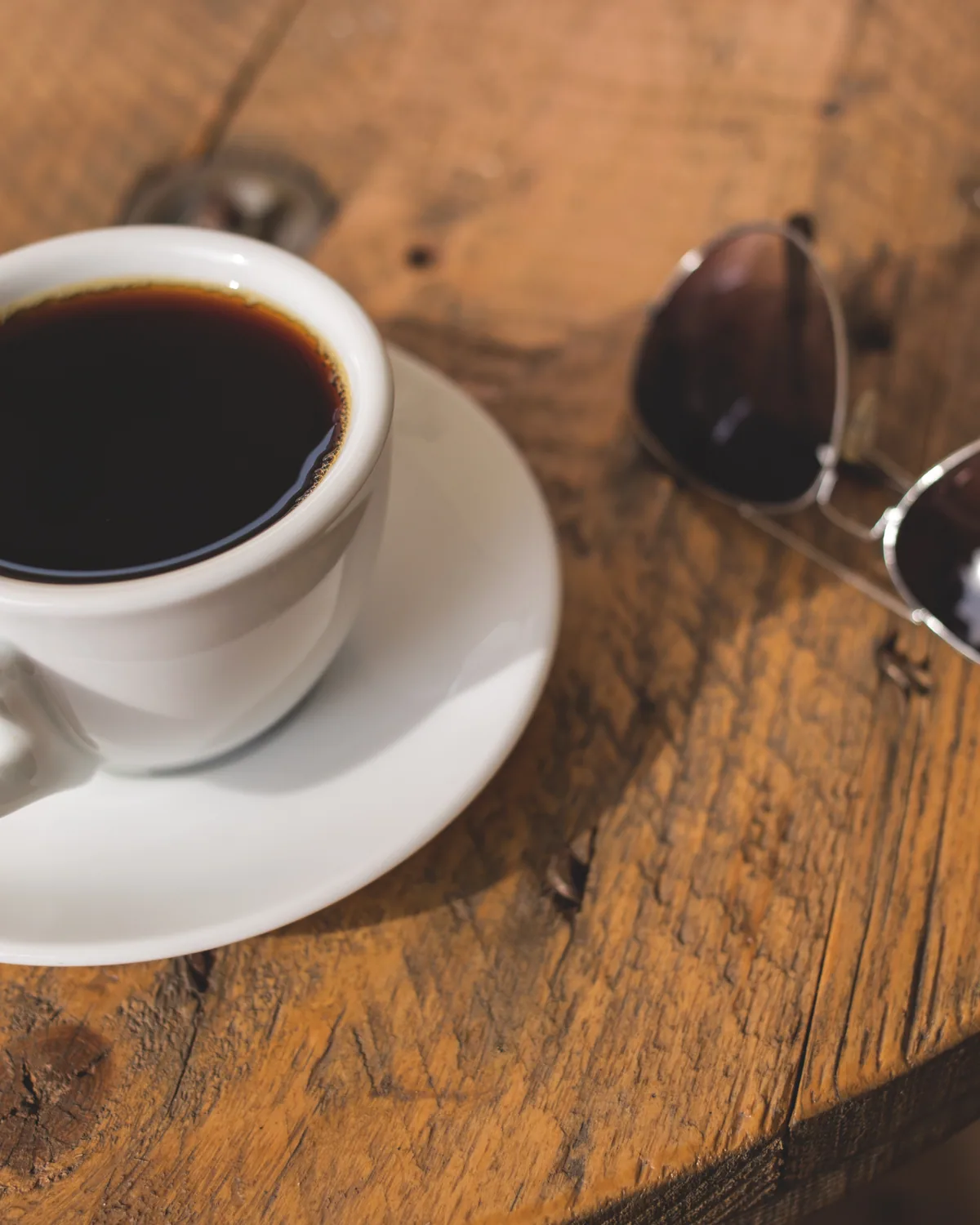 A white cup of black coffee on a saucer on a round wooden table