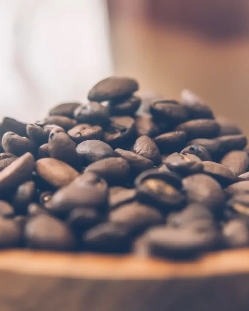 A heaped mound of roasted beans in a shallow pale wooden bowl