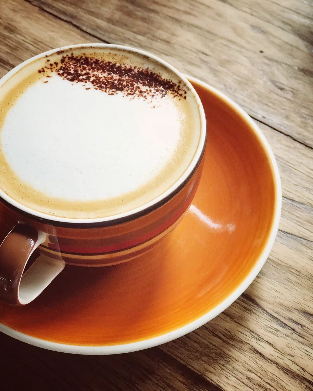 A cappuccino dusted with chocolate in a burnt-orange cup and saucer